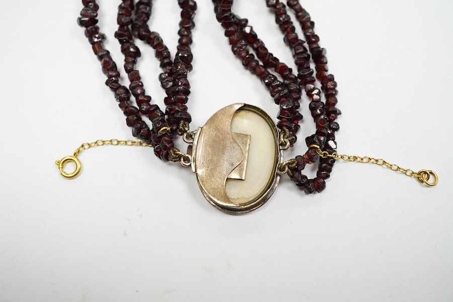 A late 19th/early 20th century multi strand rough cut garnet set necklace, with a yellow metal mounted oval cameo shell clasp, 43cm. Condition - poor to fair